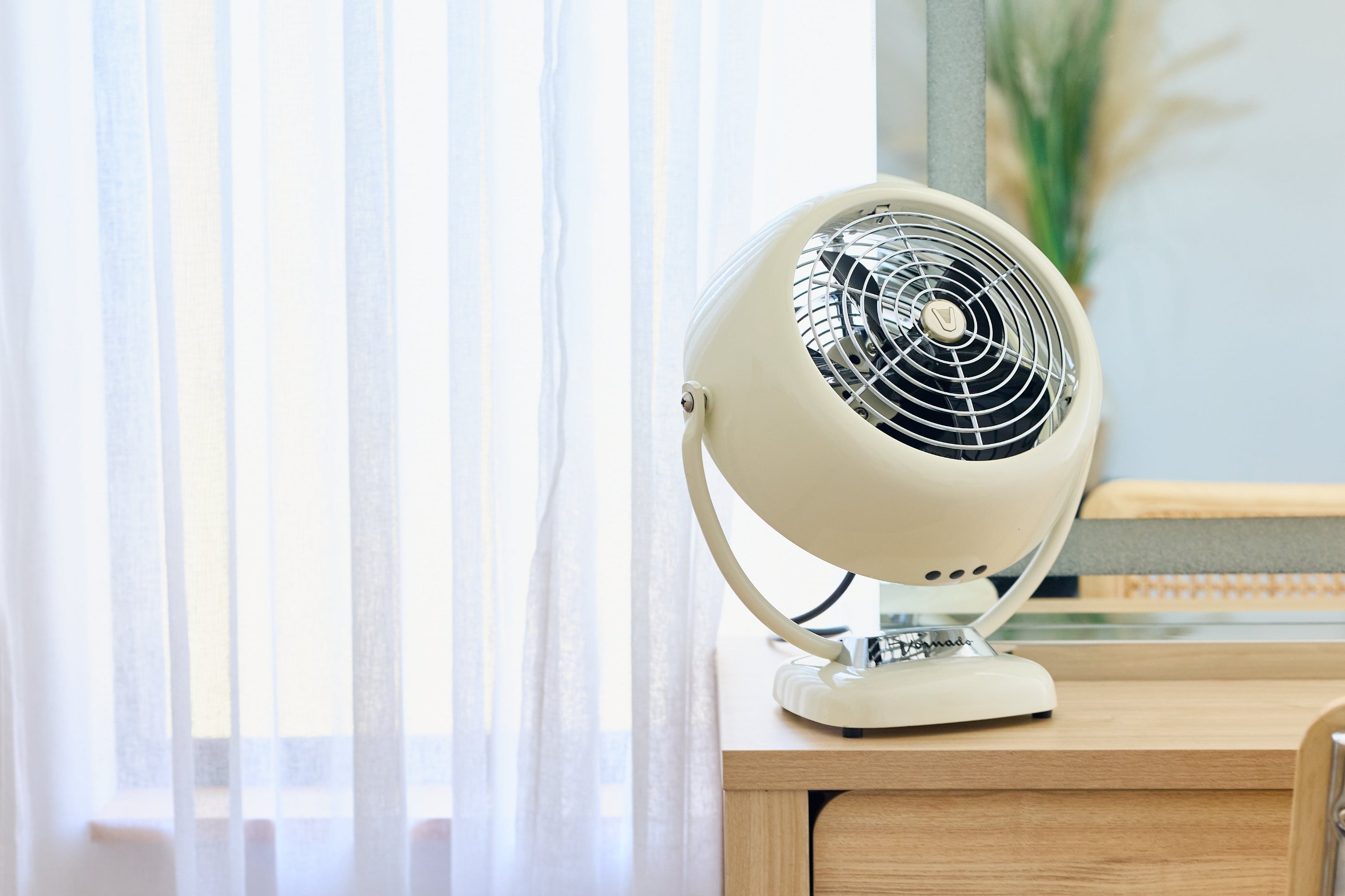Vintage-style cream-colored Vornado VFan on a wooden surface with light curtains in the background