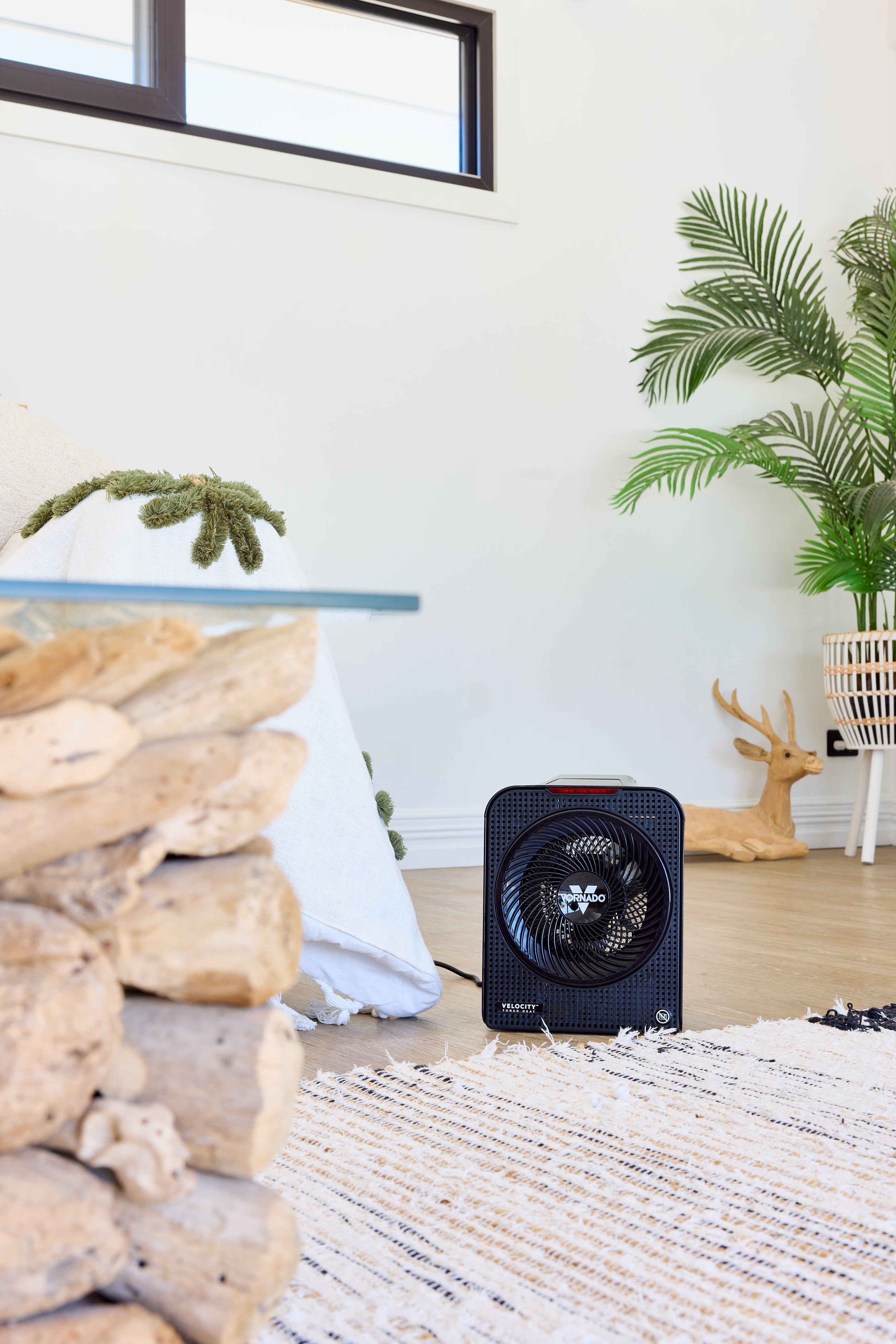 Black Vornado Velocity 5 fan heater on a wooden floor with decorative elements like rocks, plants in a living room.