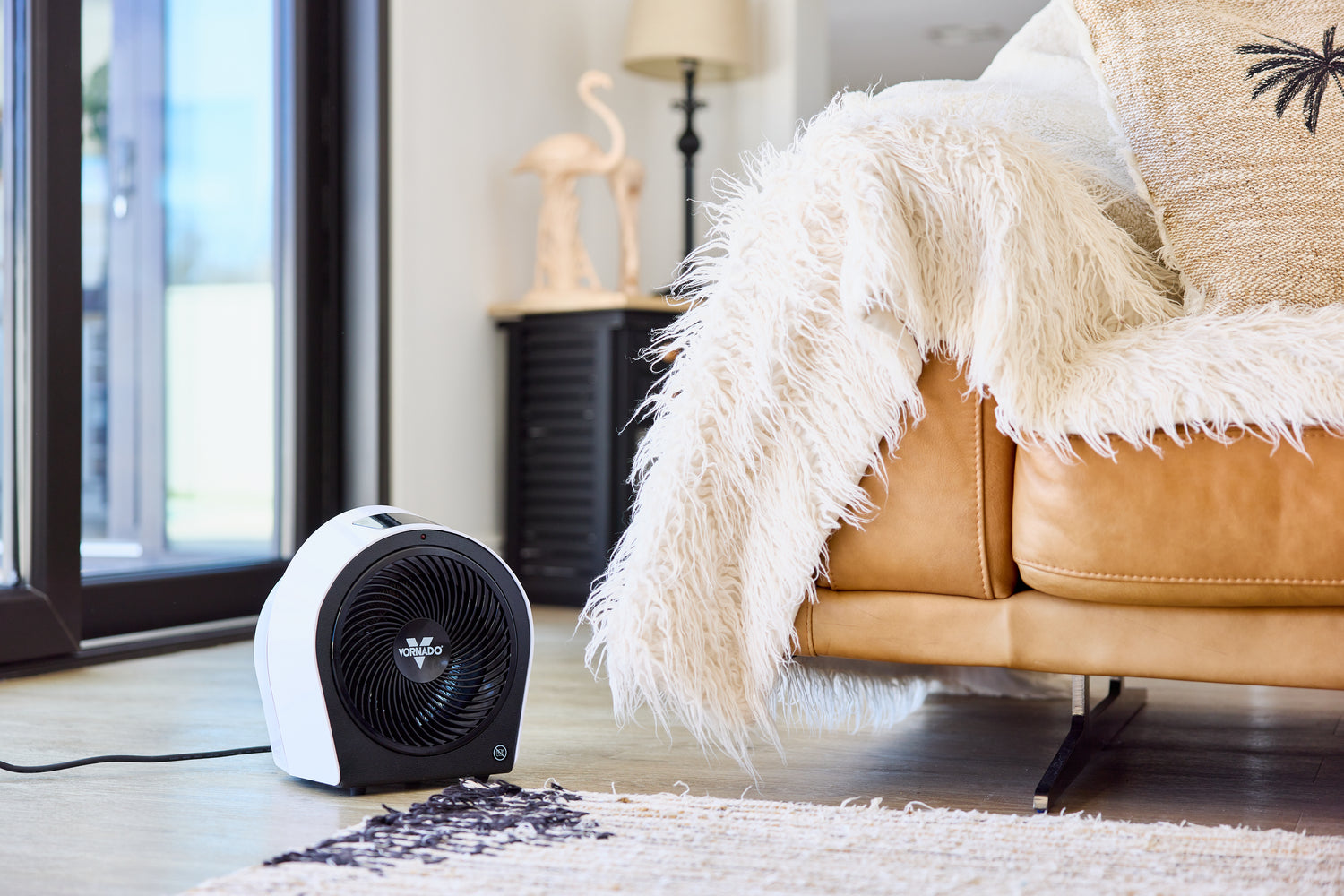 Portable space heater on a rug in a living room with a couch and lamp in the background.