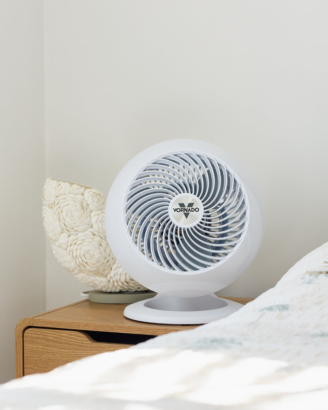 White Vornado 560 Medium Air Circulator on a wooden nightstand with a light gray wall in the background