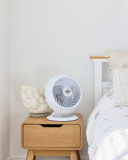 White Vornado 560 Medium Air Circulator on a wooden nightstand next to a bed with white bedding