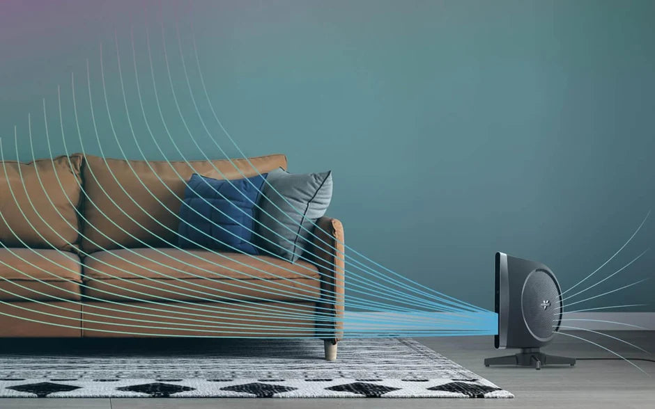 A modern room scene showing a brown leather sofa with blue and gray pillows, a patterned rug, and a STRATA Tower Fan on the right, with white and blue wave graphics depict airflow. 