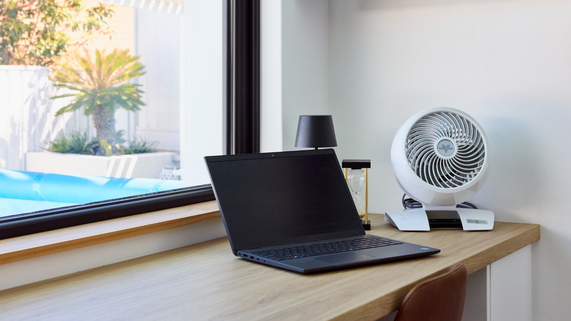Laptop on a desk next to a Vornado 5303DC Energy Smart™ Small Air Circulator with Remote with a window view of a pool and garden.